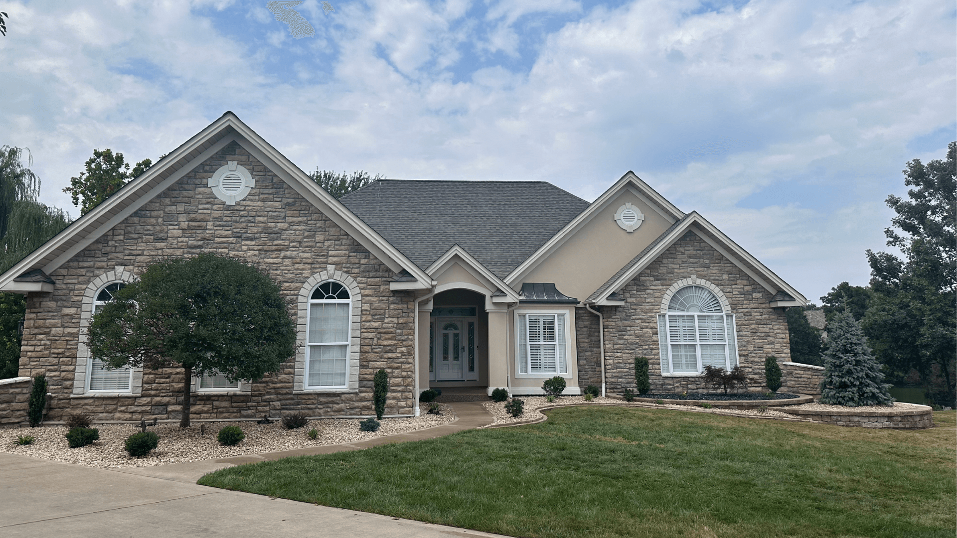 Large stone and stucco home with professional front yard landscaping curved mulch beds and evergreen shrubs by NxGen Outdoors
