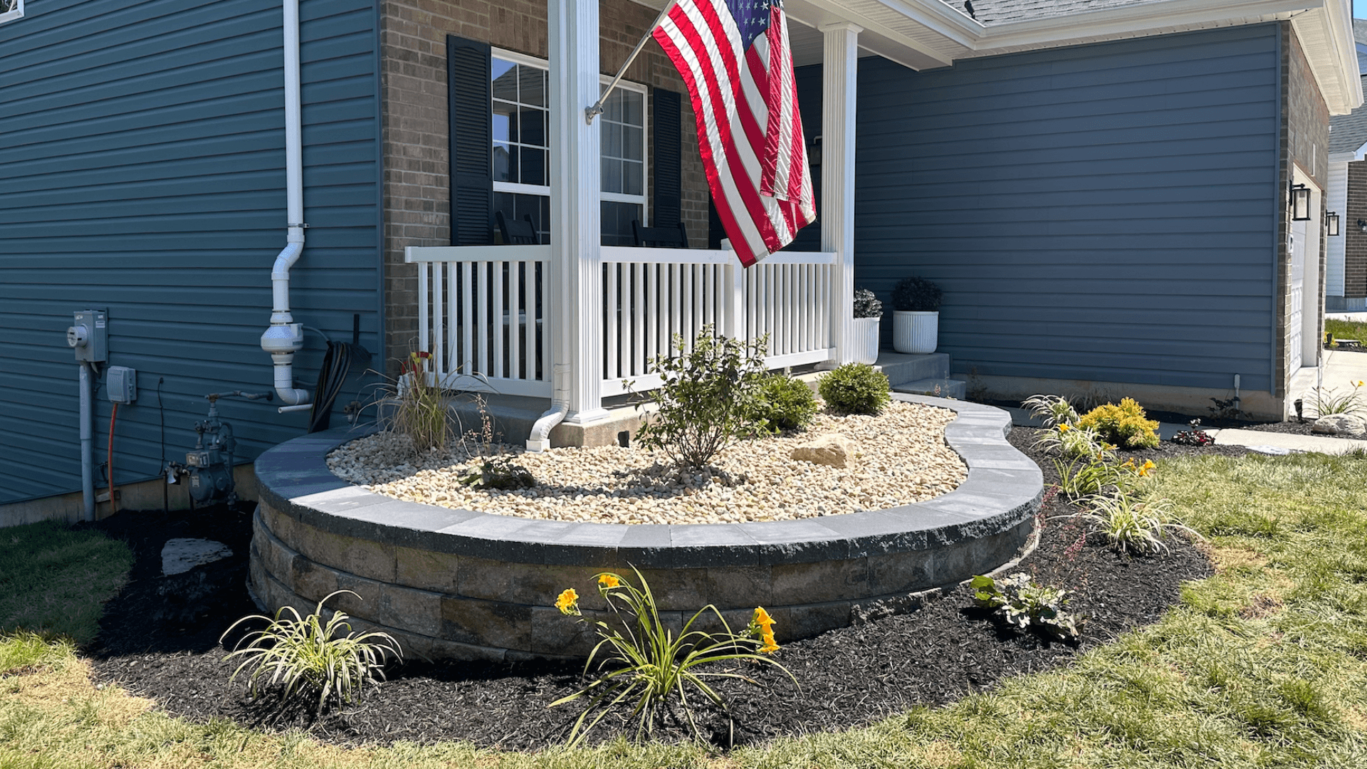 Front porch curved stone retaining wall river rock beds flower plantings and paver steps by NxGen Outdoors