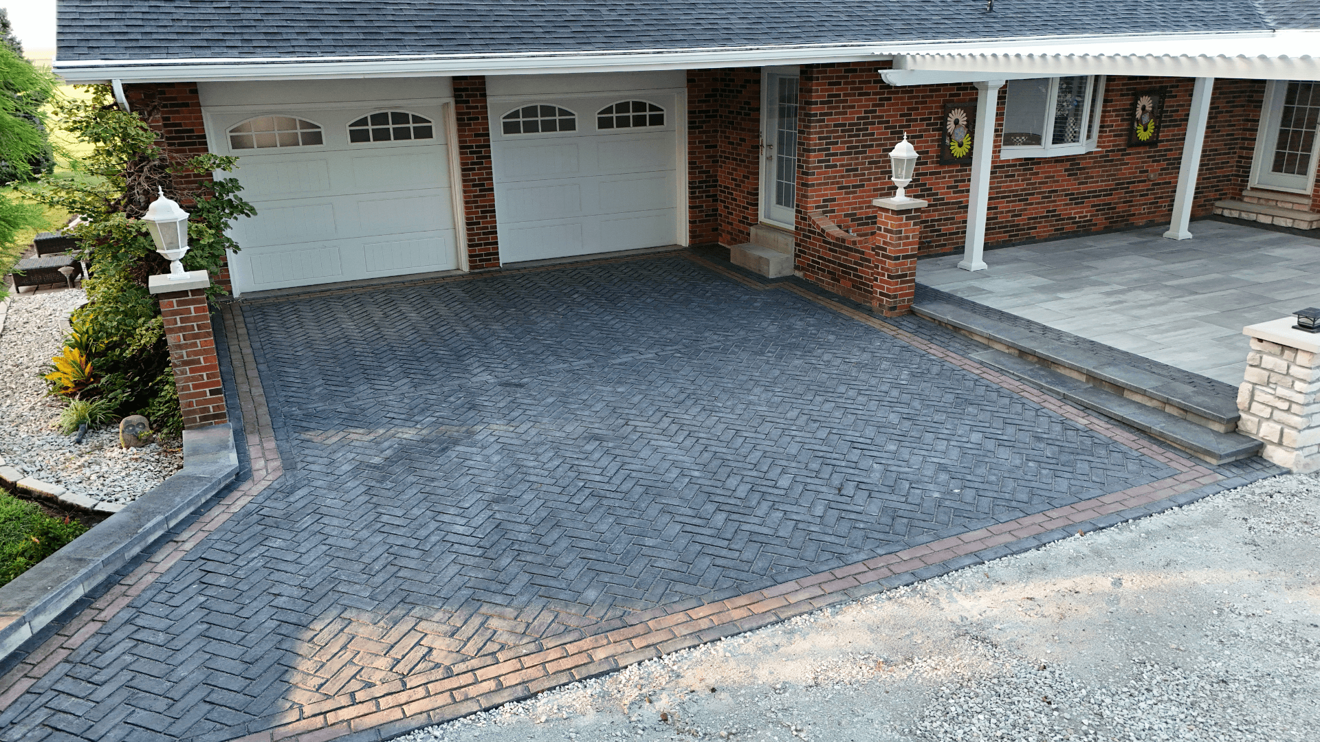 Charcoal herringbone paver driveway with red brick border accent at brick home by NxGen Outdoors