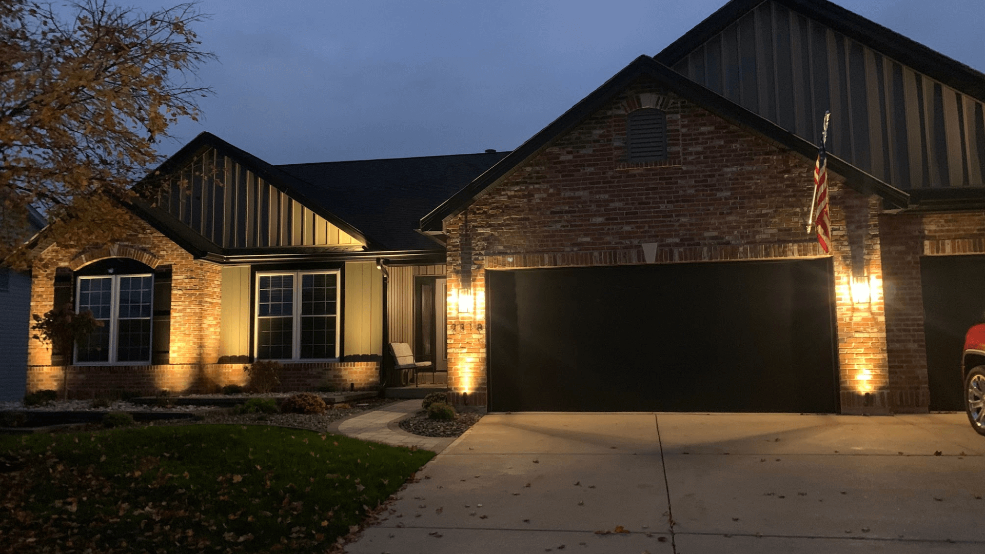 Nighttime landscape lighting highlighting brick and stone home facade and front yard by NxGen Outdoors