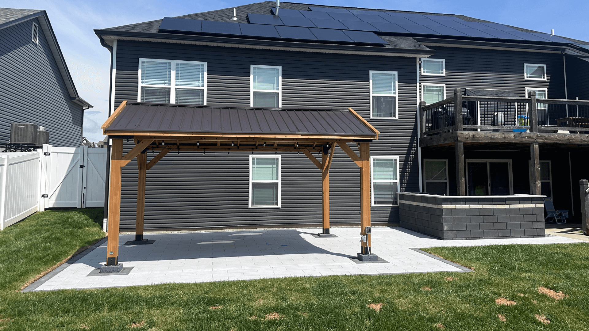 Backyard wood pavilion with metal roof paver patio and outdoor kitchen bar with stone veneer by NxGen Outdoors
