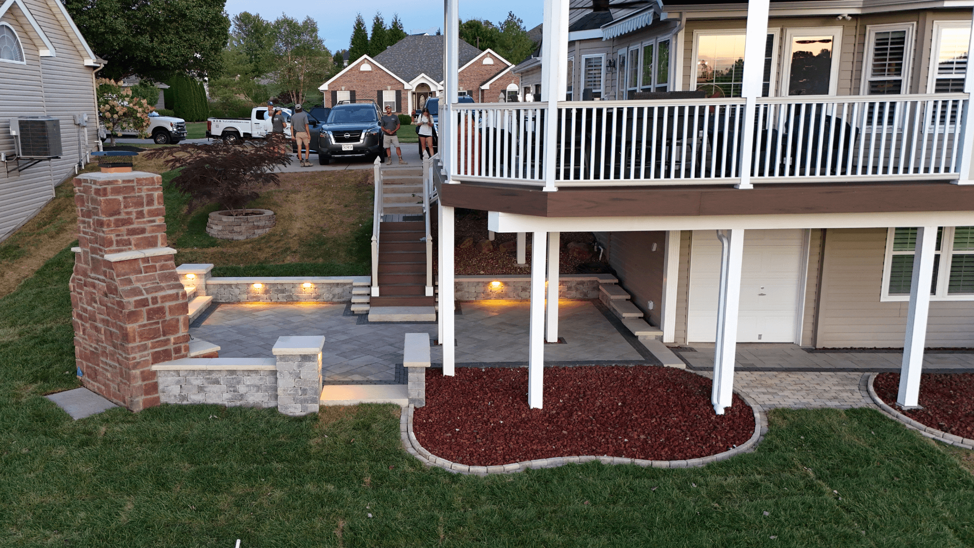 Raised deck with brick column paver steps landscape lighting and mulch beds by NxGen Outdoors