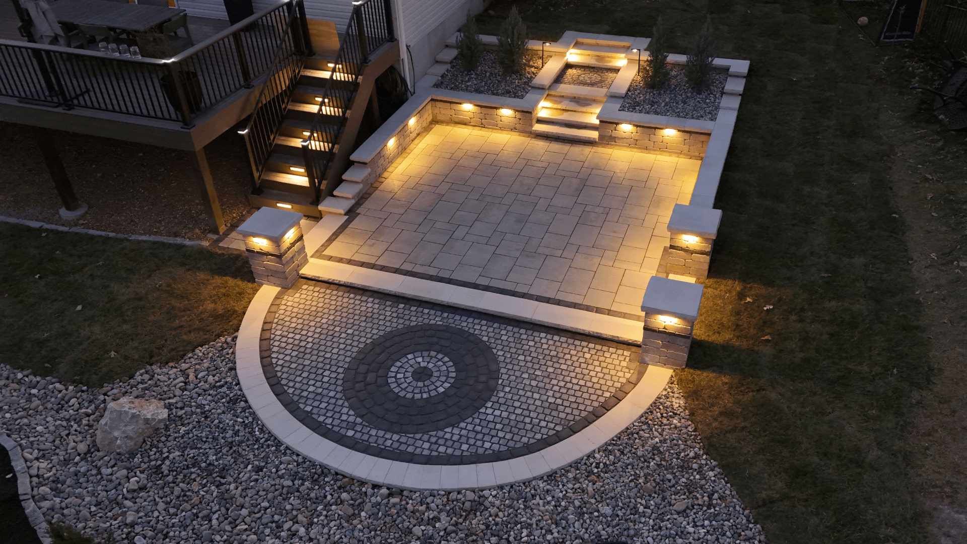 Nighttime paver patio with circular medallion landscape lighting on pillar caps and step lights by NxGen Outdoors
