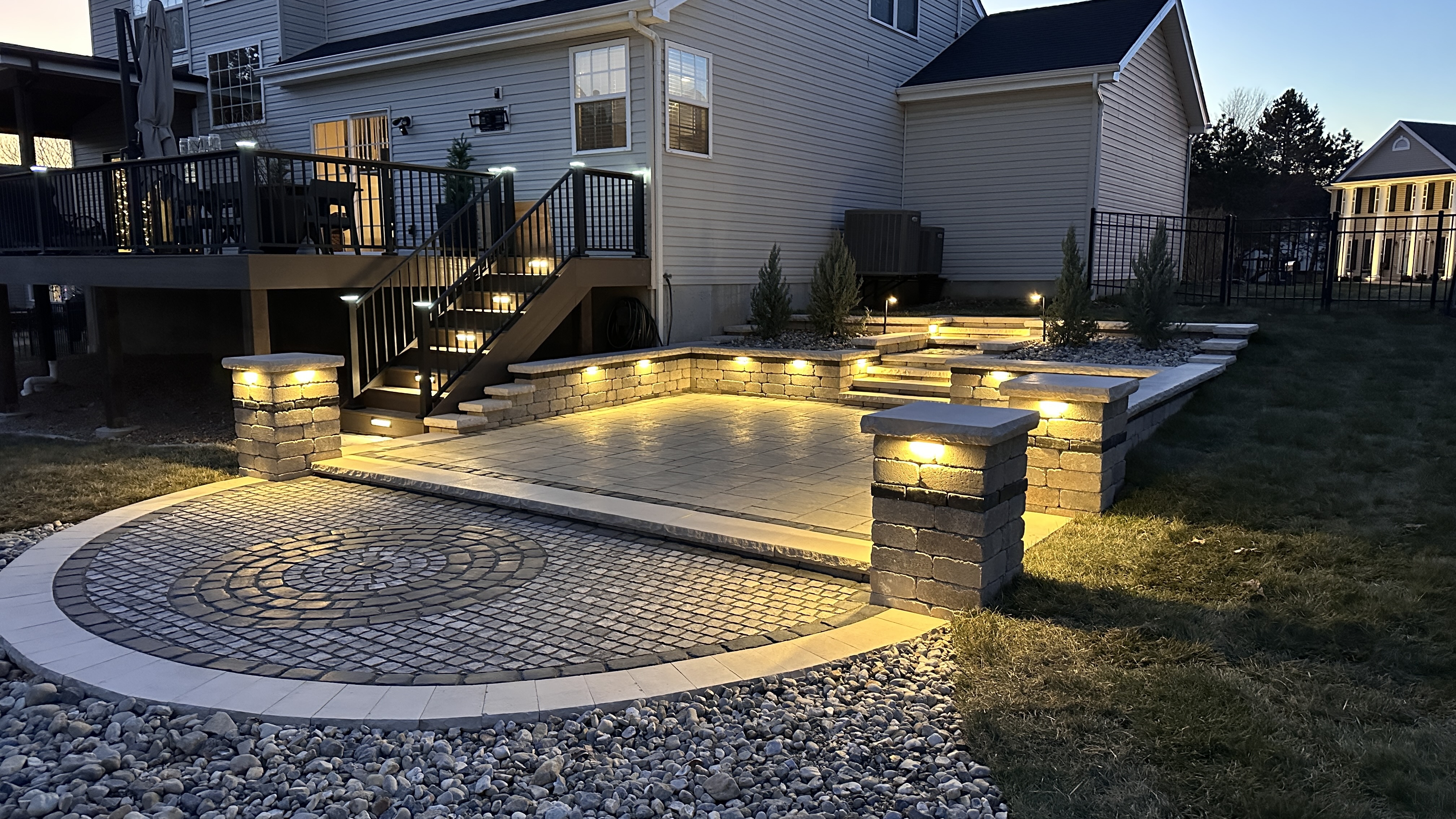 Curved paver patio with landscape lighting, stone pillars, and step lights illuminated at night