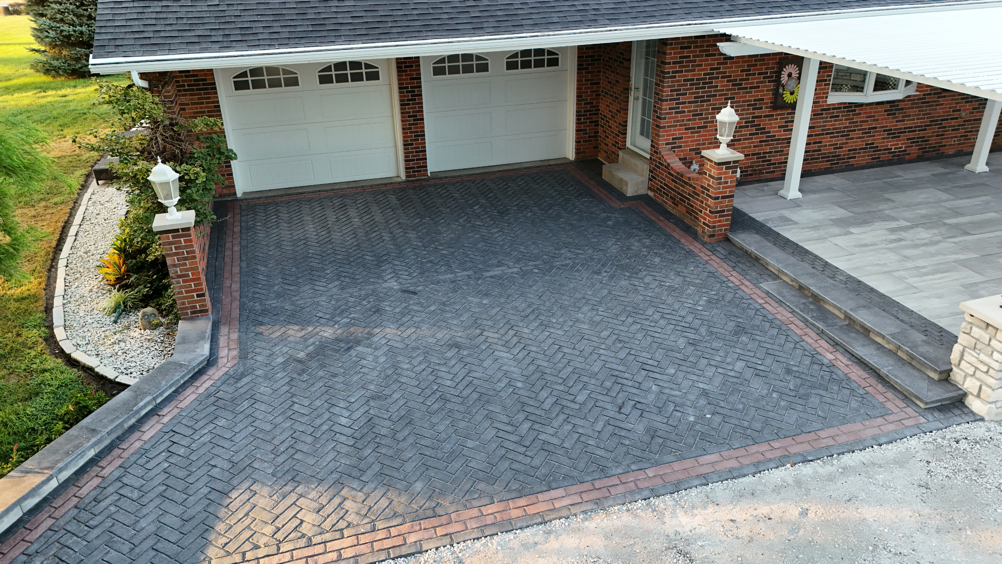 Paver driveway with brick border accents leading to covered front porch with stone columns and lanterns