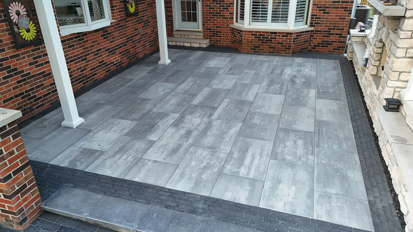Wide angle view of covered patio with large format paver flooring white pergola columns and stone accents